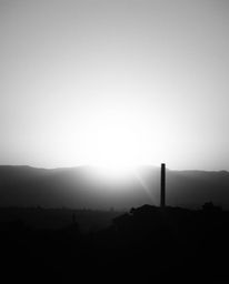 A timeless and elegant black and white photograph depicting a sunrise over a war-torn landscape. The intense dramatic lightin
