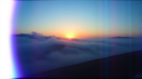 A cinematic image capturing fog-covered hills bathed in a vibrant sunset light. The scene employs a cool color palette domina
