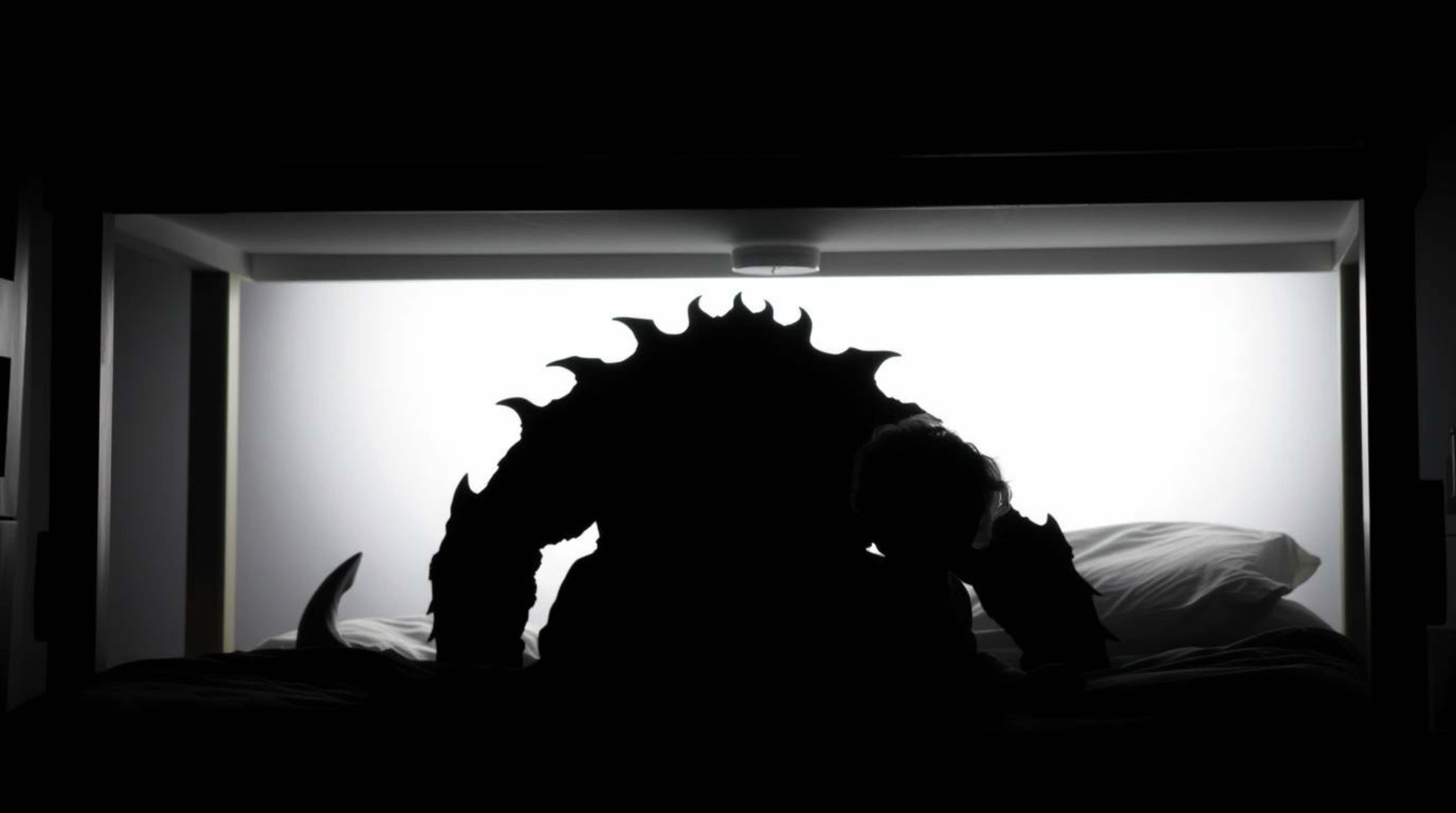 A captivating image depicts a jet-black monster, silhouetted under a bed, forming an unlikely friendship with a child.  The i