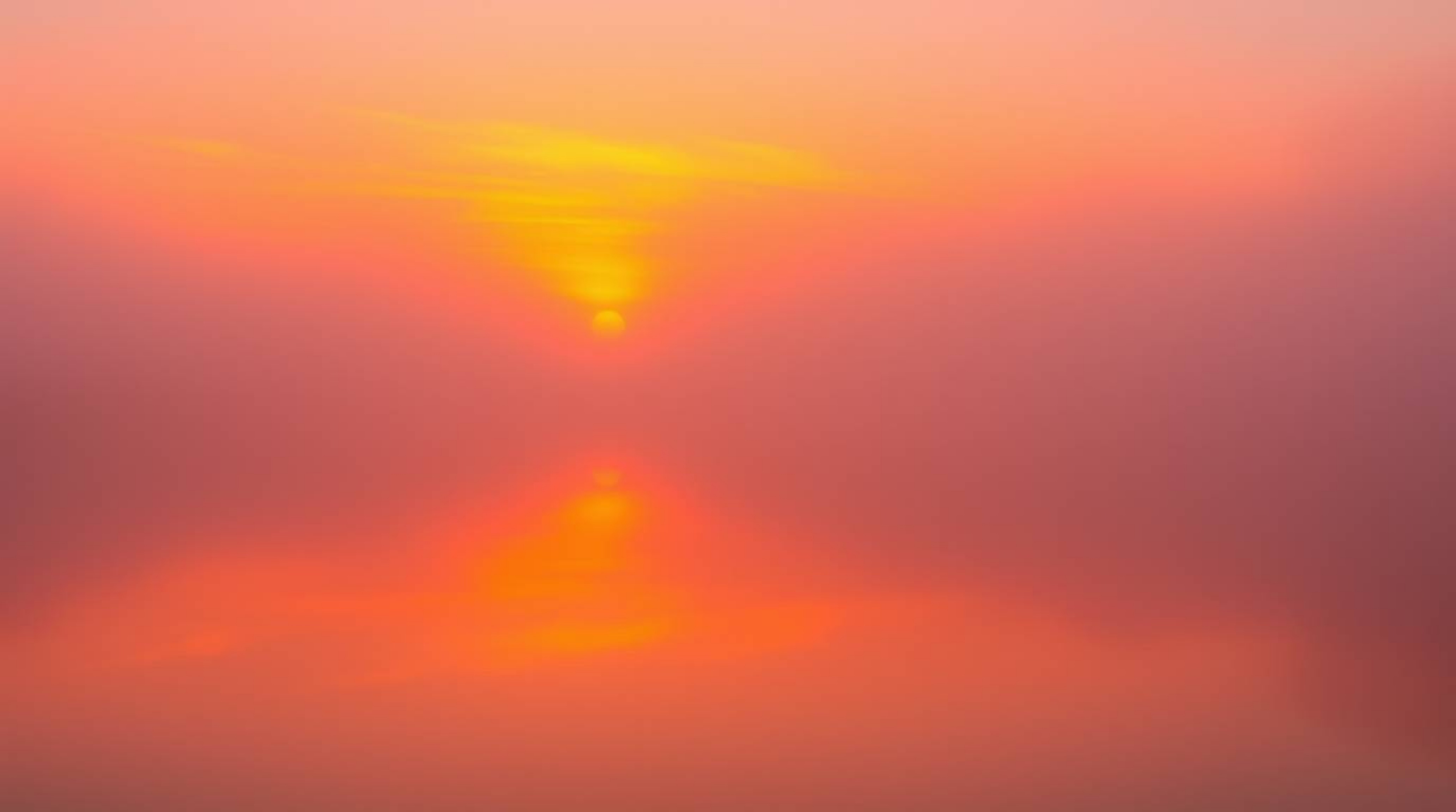 A mesmerizing scene unfolds: a vibrant sunset casts its fiery hues onto a tranquil pond, the entire landscape veiled in a thi