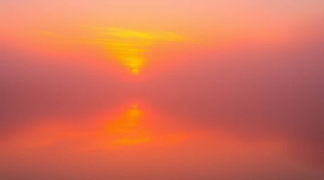 A mesmerizing scene unfolds: a vibrant sunset casts its fiery hues onto a tranquil pond, the entire landscape veiled in a thi