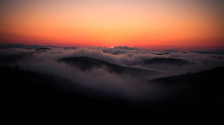 A captivating close-up showcases fog-covered hills bathed in the golden light of a dramatic sunset.  The image boasts high co