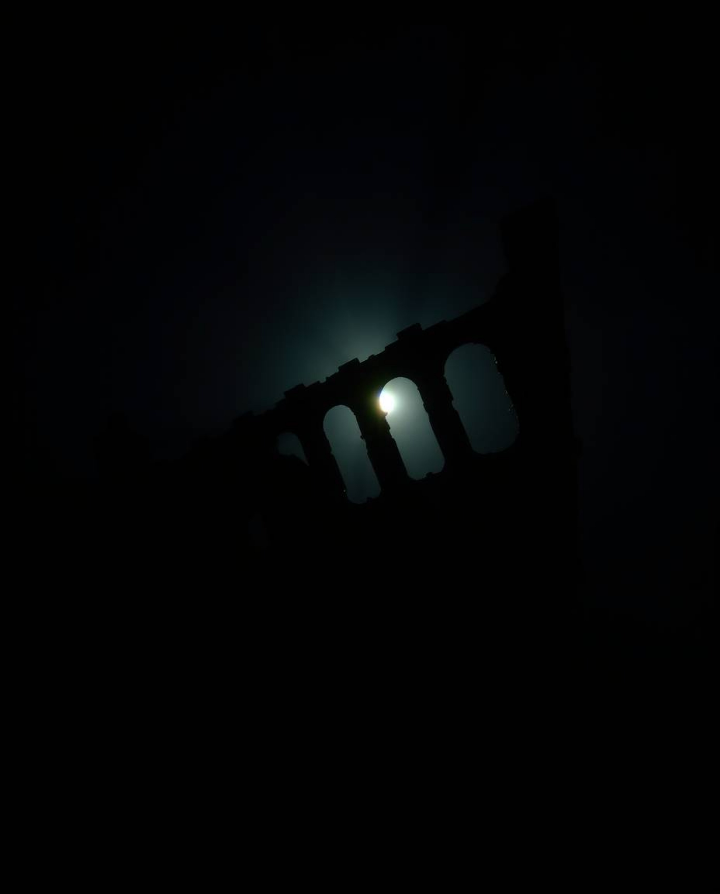 A silhouetted shipwreck, beautifully illuminated deep underwater, creates a captivating scene. The backlighting effect emphas