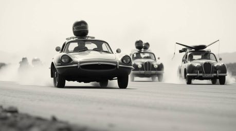 A classic black and white photograph showcasing a wacky racing scene with outlandish cars.  The image is enhanced with a soft